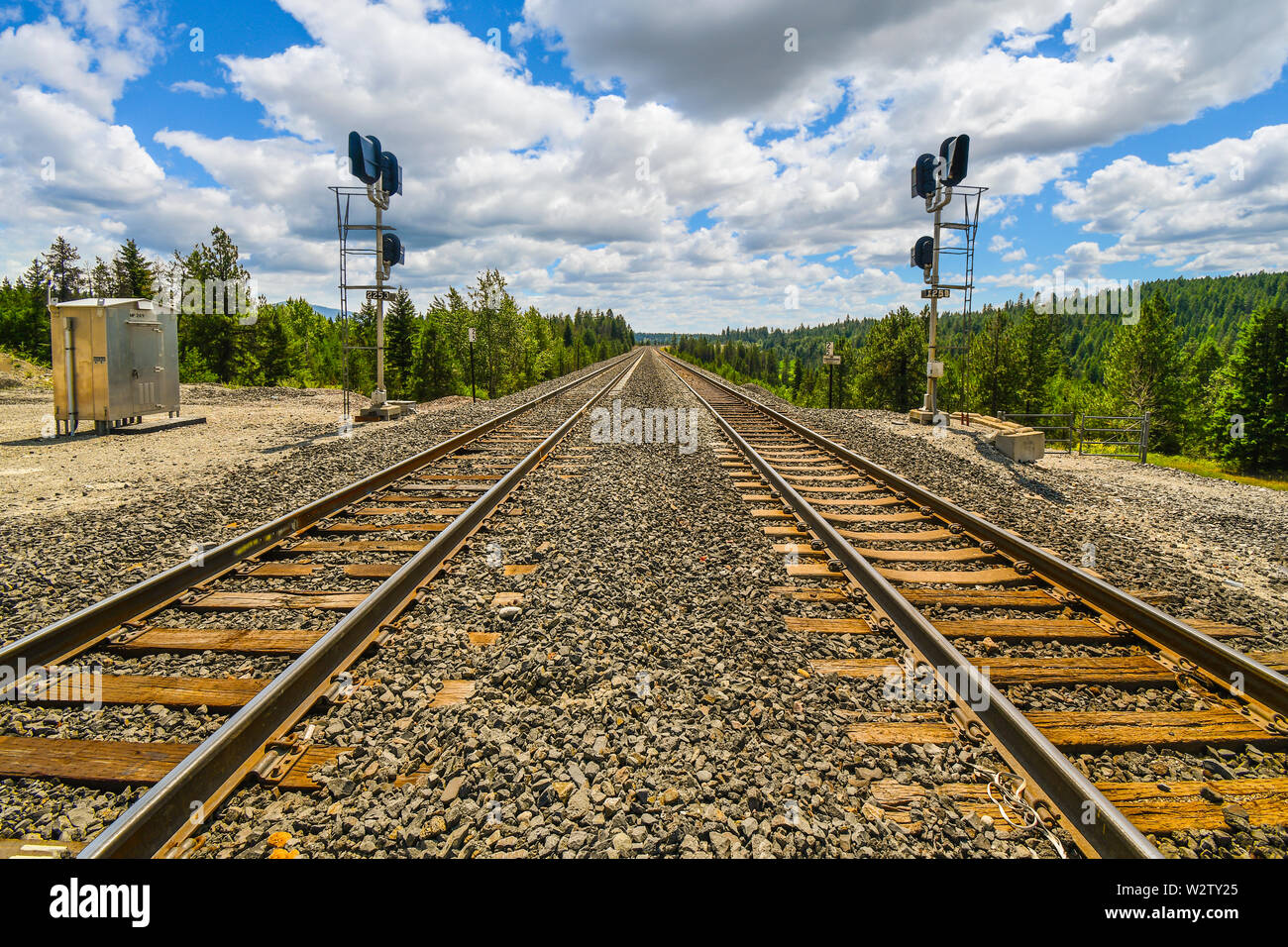 A long straight set of railroad train tracks disappear in the horizon through the mountains in the rural Inland Northwest area of North Idaho. Stock Photo