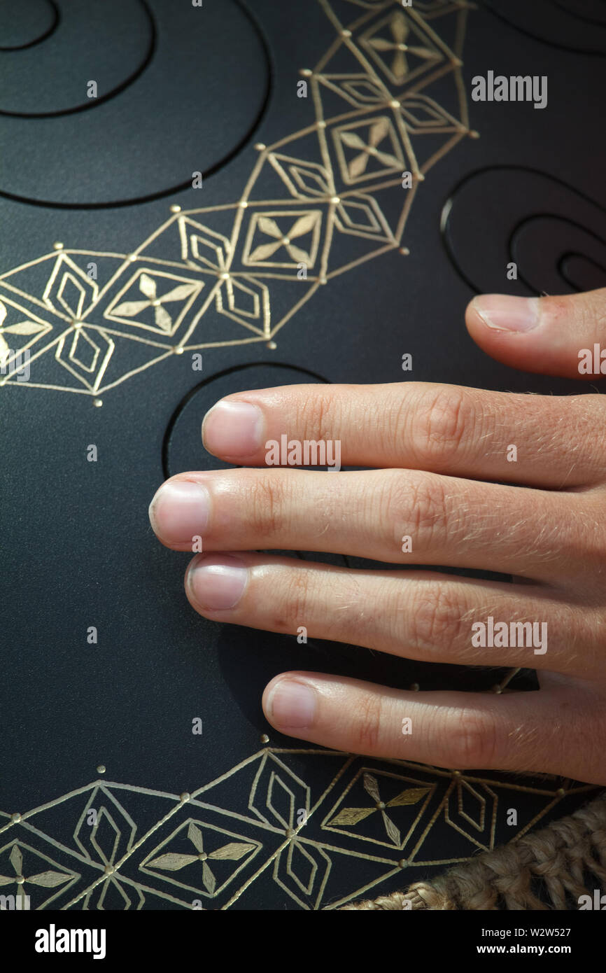 Closeup of a mans hand playing on modern musical instrument Hand pan or Vadjraghanta or metal tongue drumon, selective focus Stock Photo