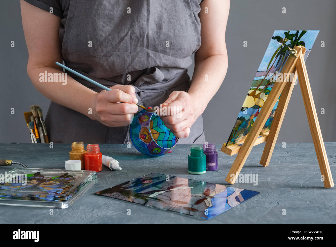 Painter holding a paintbrush in his hand and painting with stained glass paints on a glass vase. Stock Photo