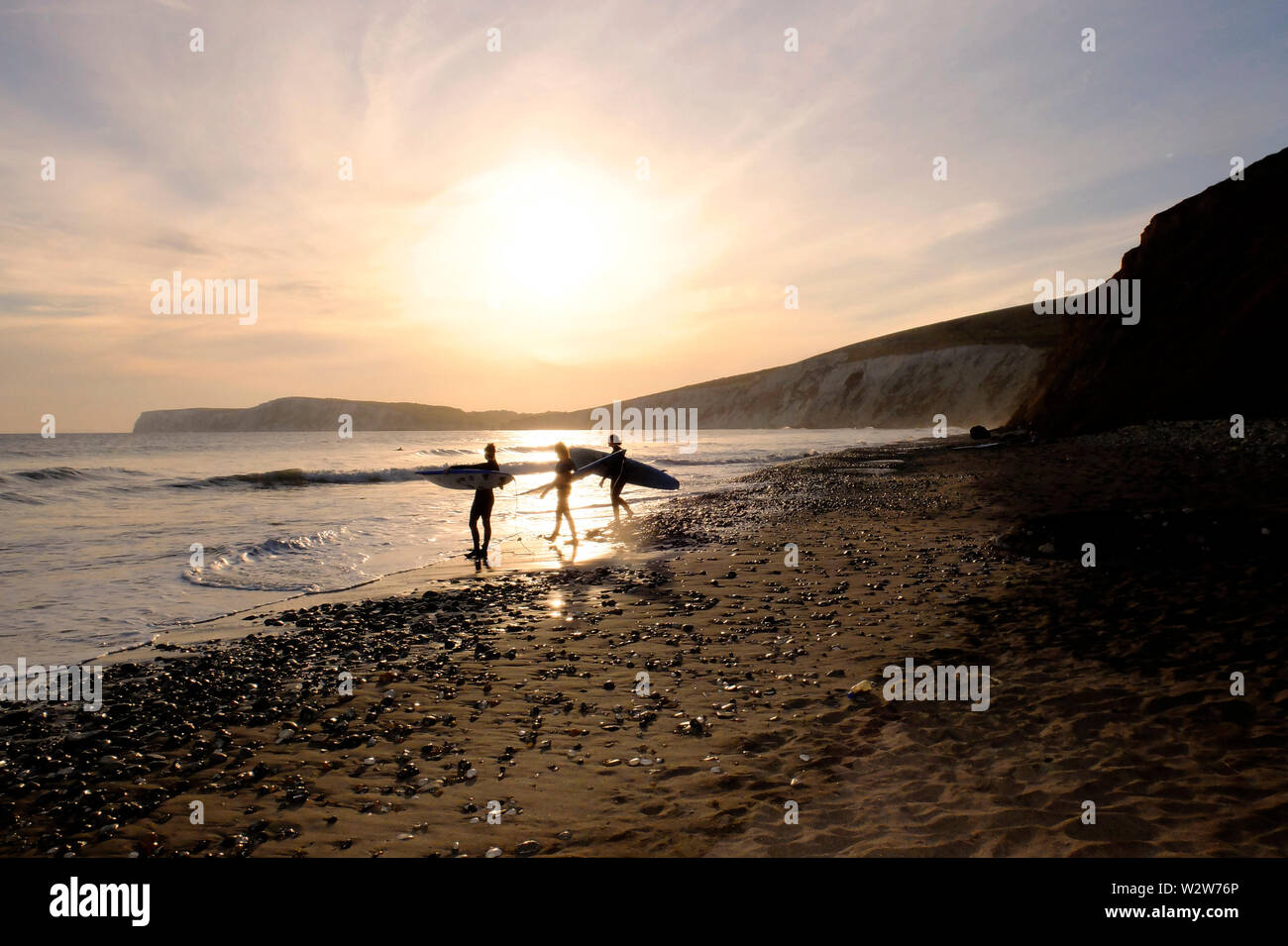 A group of young women surfers head out along the seashore in the surf ...