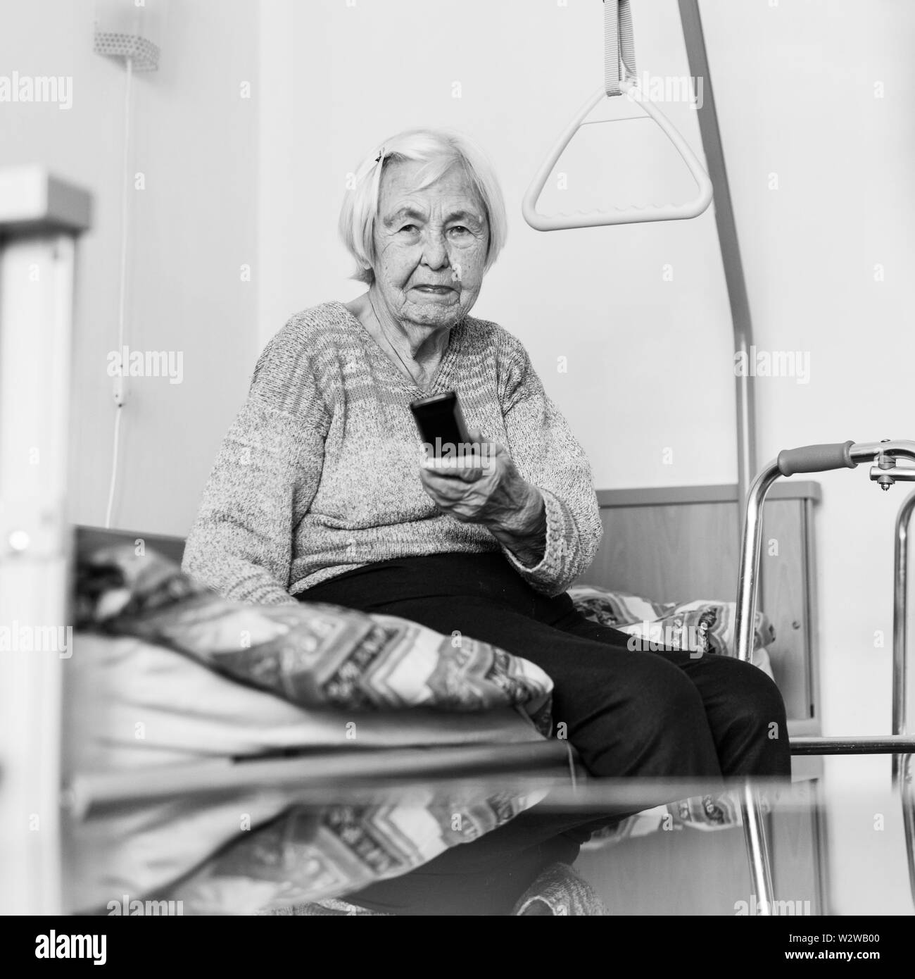 Elderly 96 years old woman operating TV or DVD with remote control in black and white. Stock Photo