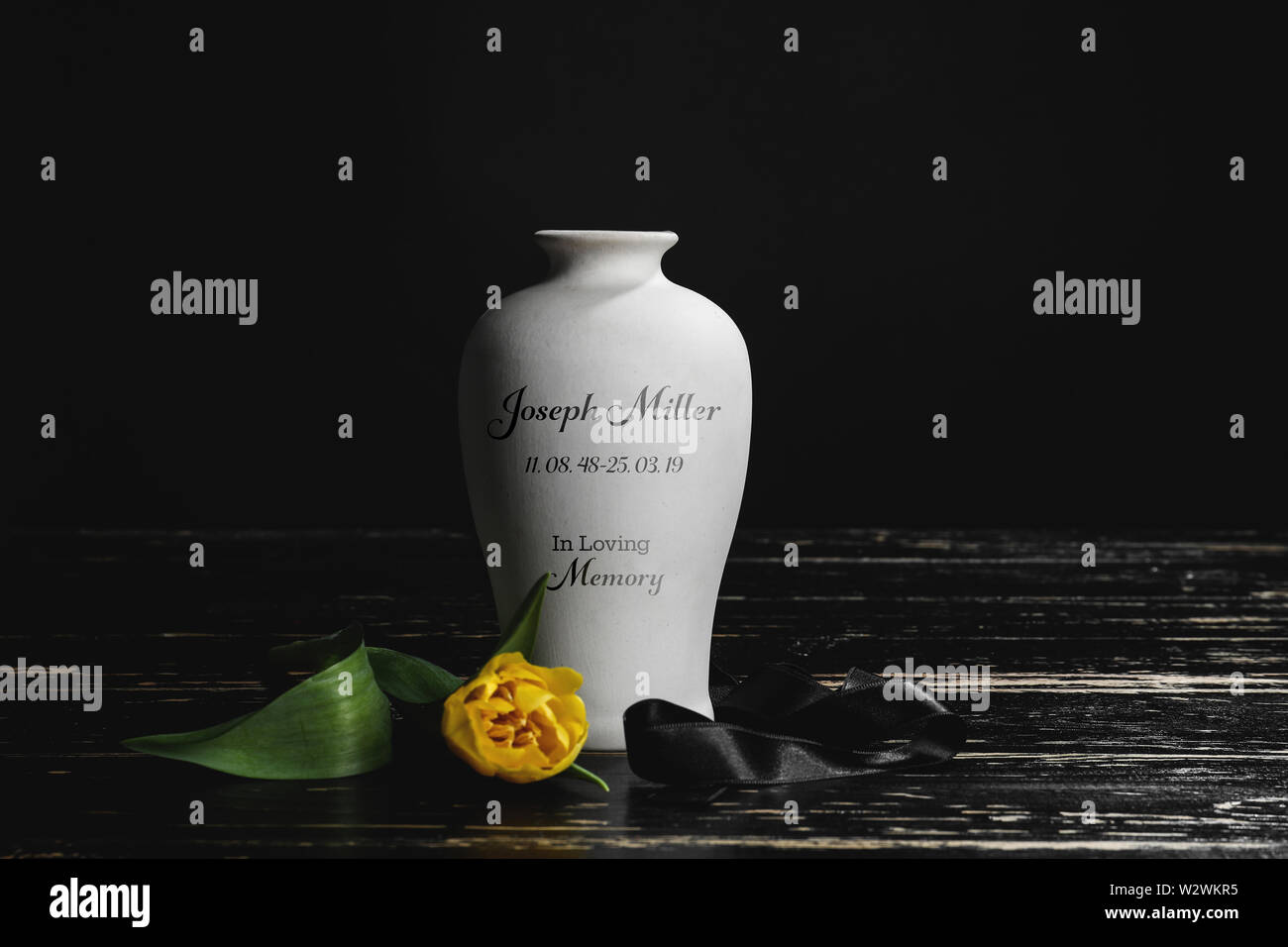 Mortuary urn with ribbon and flower on table against dark background