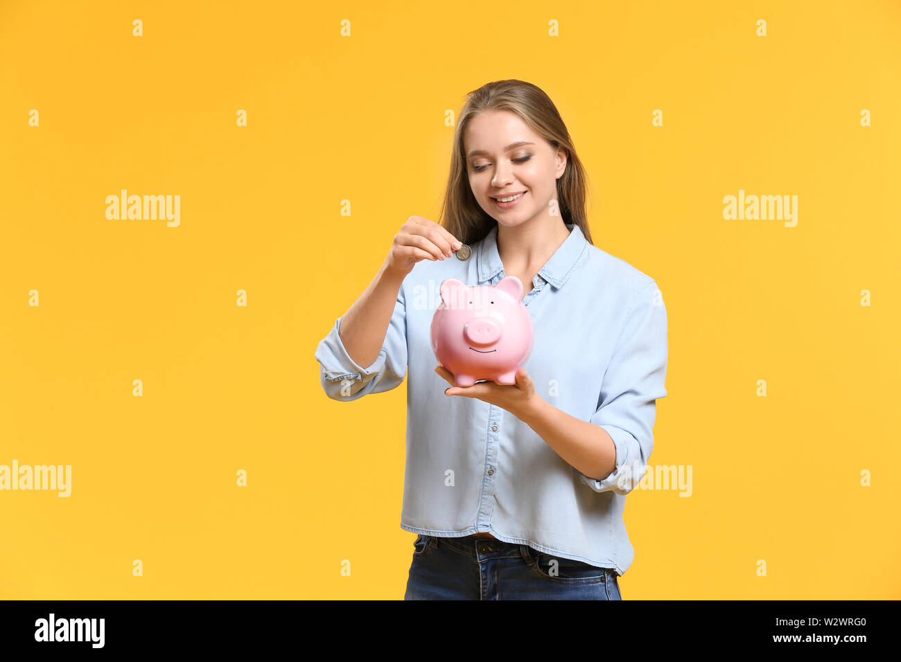 Young woman putting coin into piggy bank on color background Stock ...