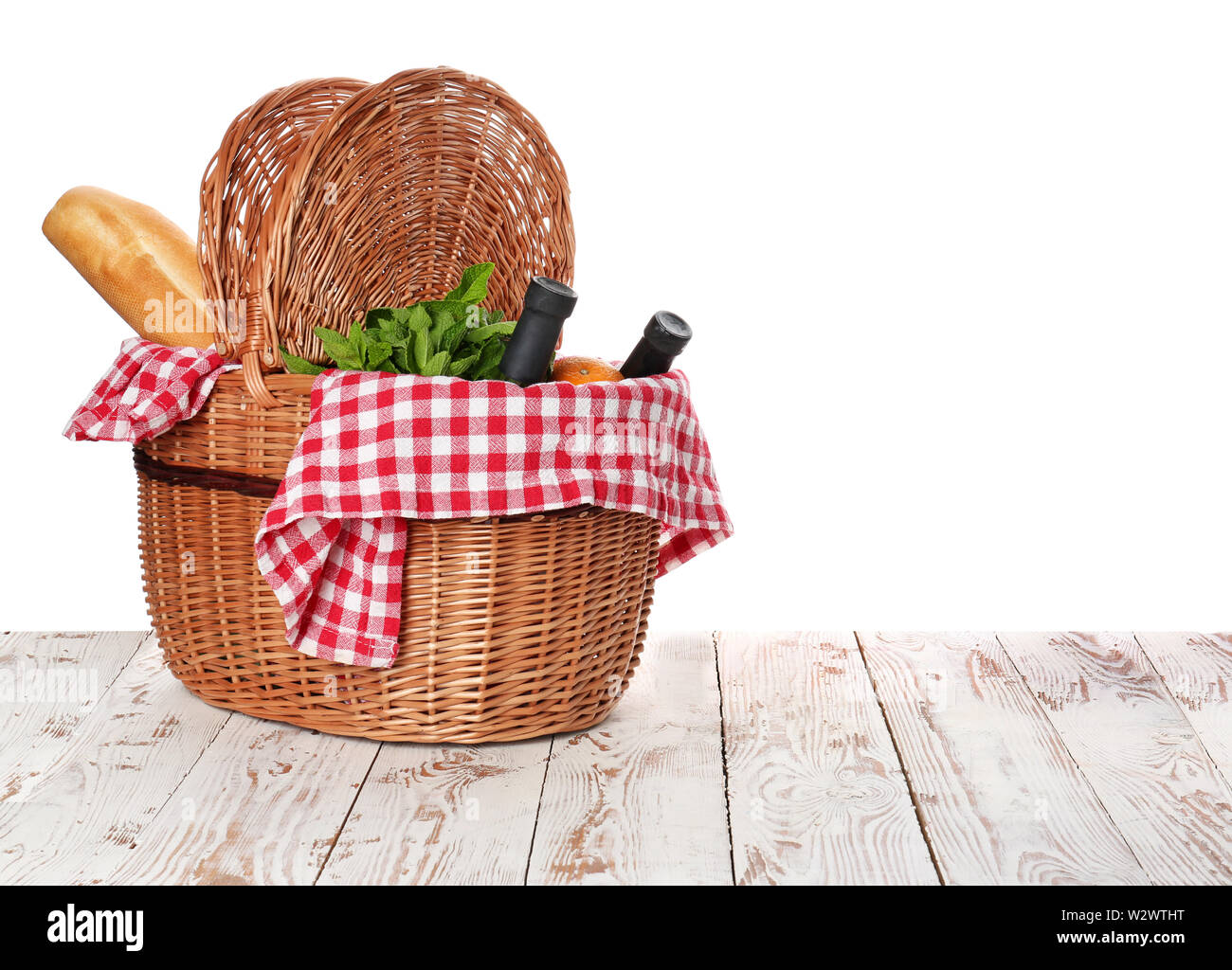 Wicker basket with tasty food and drink for picnic on wooden table ...