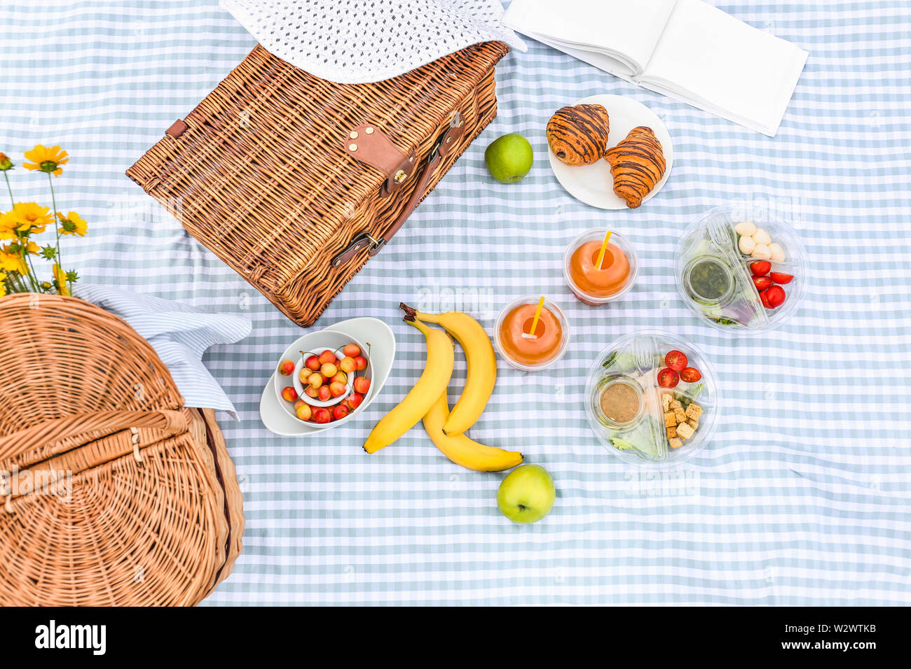 Wicker baskets with tasty food and drink for romantic picnic on plaid ...