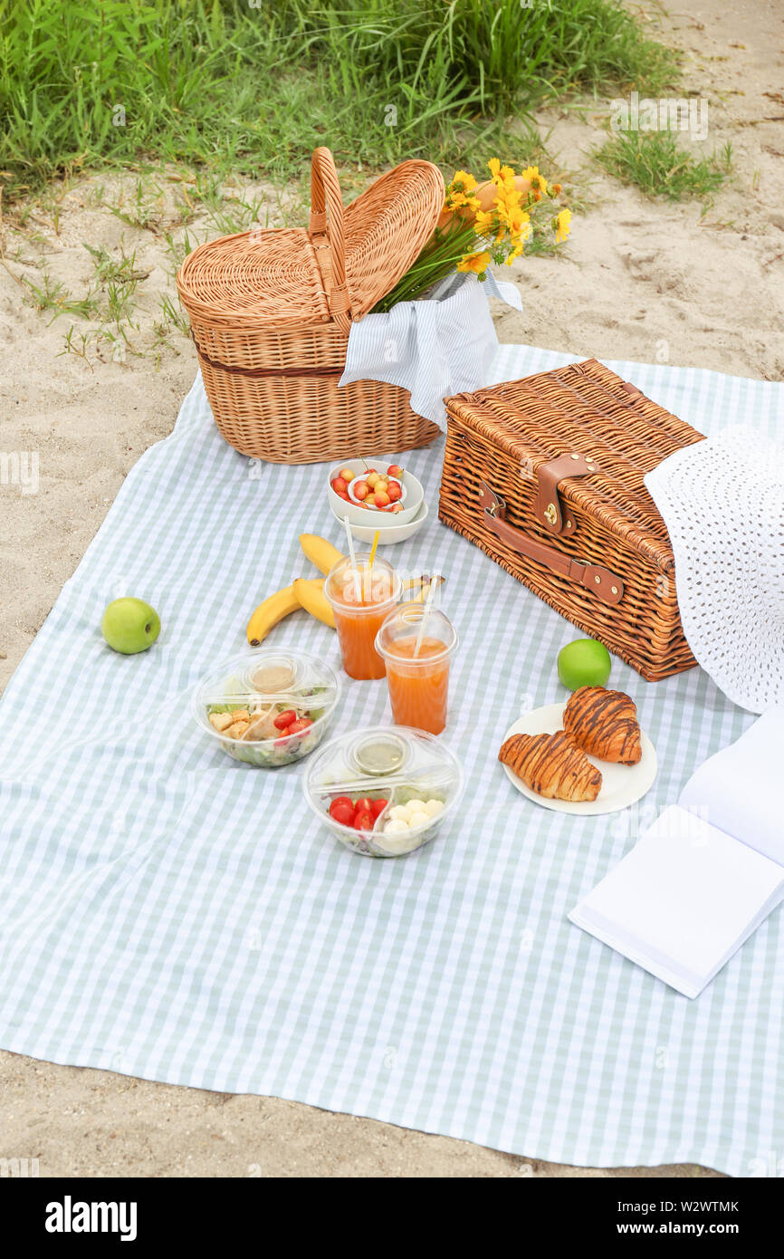 Wicker baskets with tasty food and drink for romantic picnic on beach ...