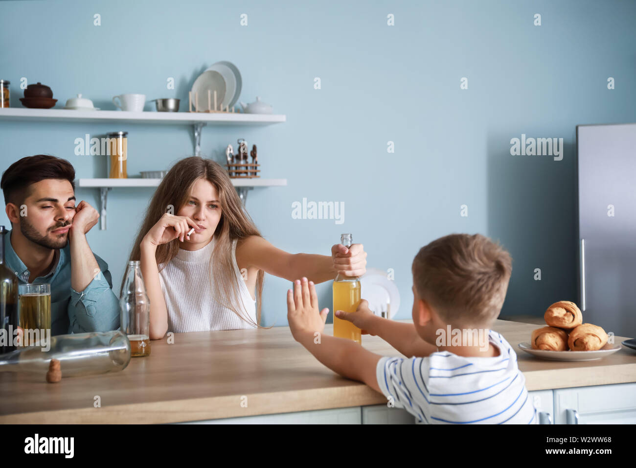 Mother offering alcohol to little son in kitchen at home. Concept of addiction Stock Photo