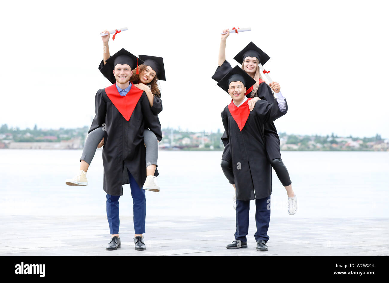 Happy students in bachelor robes and with diplomas outdoors Stock Photo