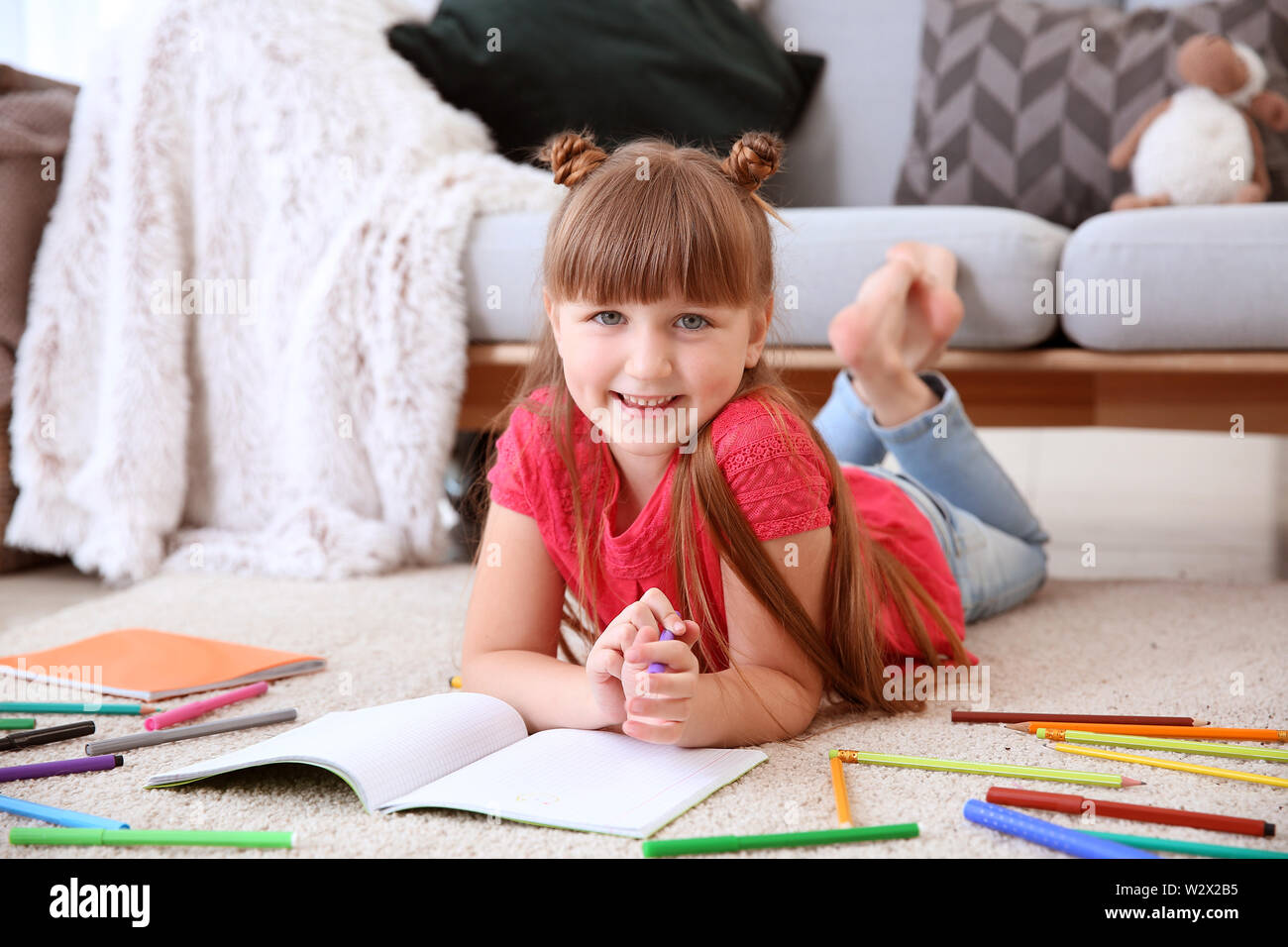 Cute little girl drawing while lying on carpet Stock Photo - Alamy