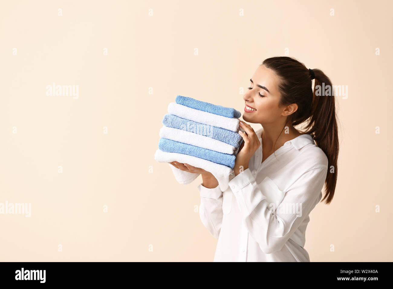 Beautiful young woman with stack of clean towels on light background ...