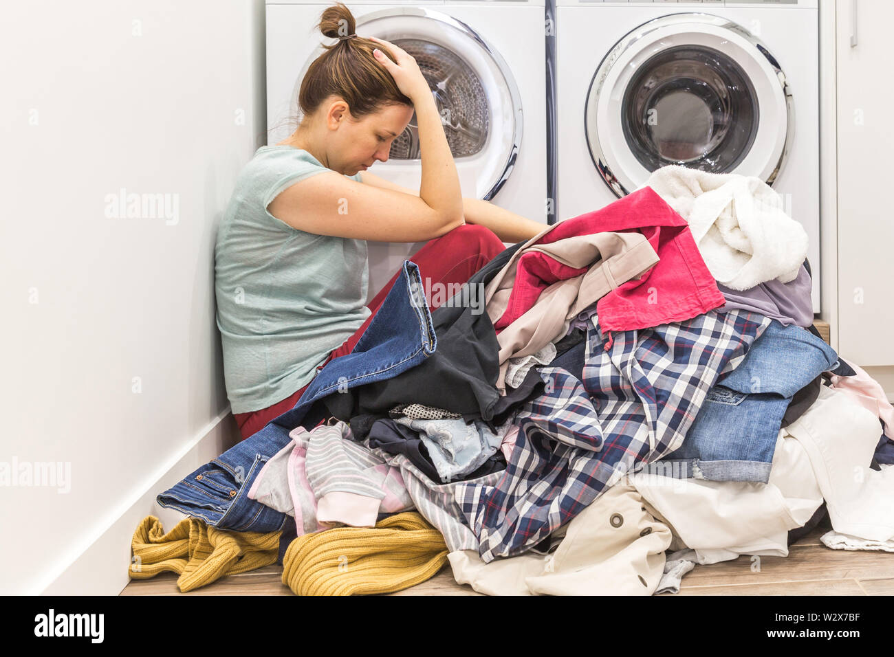 Upset woman in laudry room sitting ona floor with dirty clothes, tired and  frustrated Stock Photo - Alamy, image size:1300x956