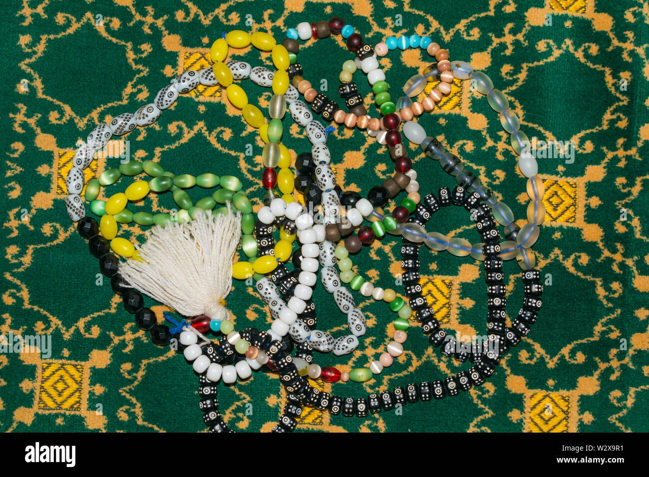 close up of multicolor muslim prayer beads on a prayer mate.multi color islamic prayer beads on ja e nmaz (prayer mate),green background. Stock Photo