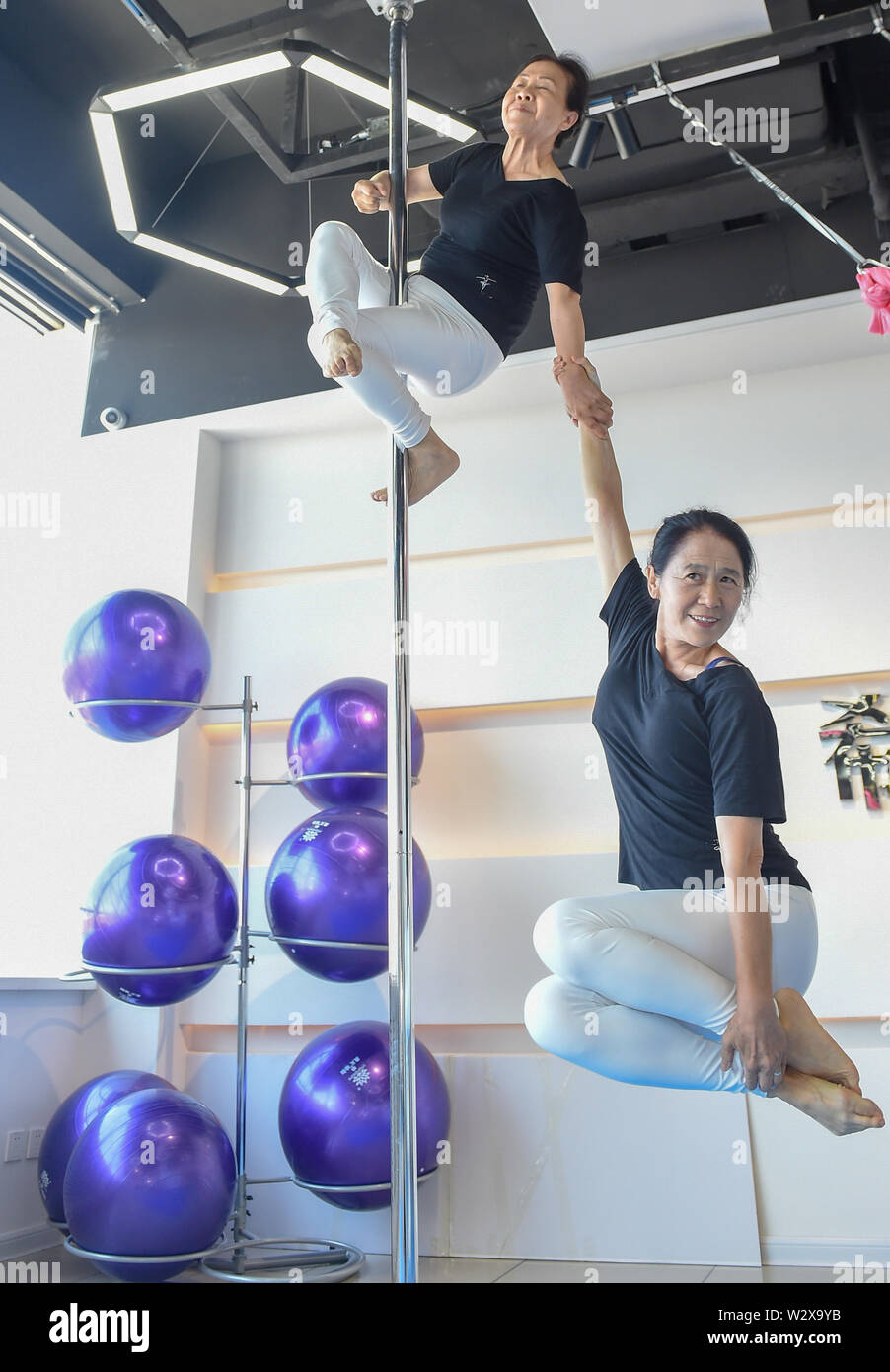 (190711) -- JILIN, July 11, 2019 (Xinhua) -- Jiang Zhijun (top) and Li Fengmei practice pole dancing in the dance room in Jilin City, northeast China's Jilin Province, July 10, 2019. A group of dama, refering to the legions of usually middle aged women, formed a team of pole dancing in Jinlin City, northeast China's Jilin Province in 2016. The team has eight members with an average age of 64. "Pole dancing is known for its softness and strength,"says Jiang Zhijun, the 68-year-old team leader." We started with basic strength training, then went forward to perform high-level moves gradually." Th Stock Photo