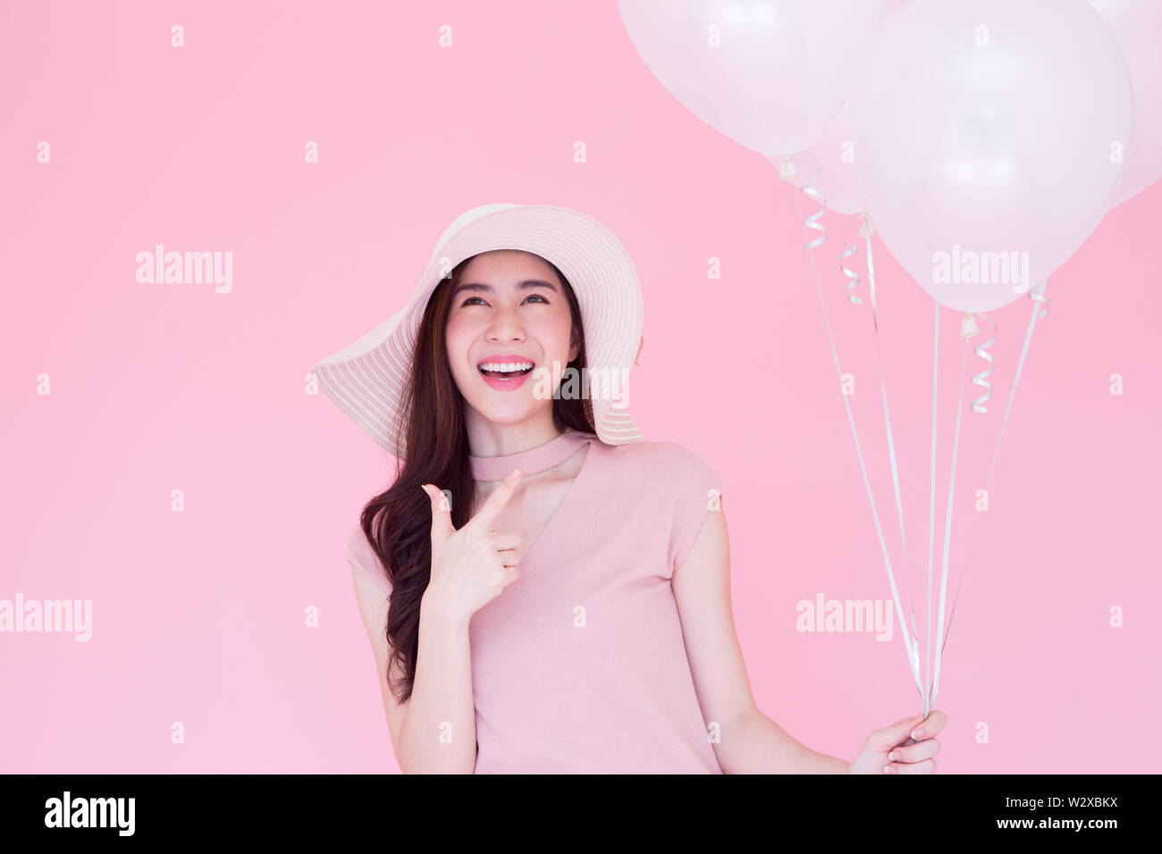 Happy beauty girl laughing with white balloons on pink background, Young woman celebrating on birthday party or having fun in holiday, Asian thai mode Stock Photo