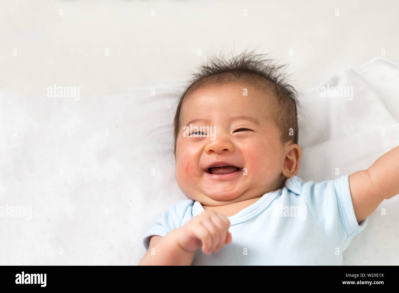 Happy little Asian baby smiling while lying on white bed Stock Photo