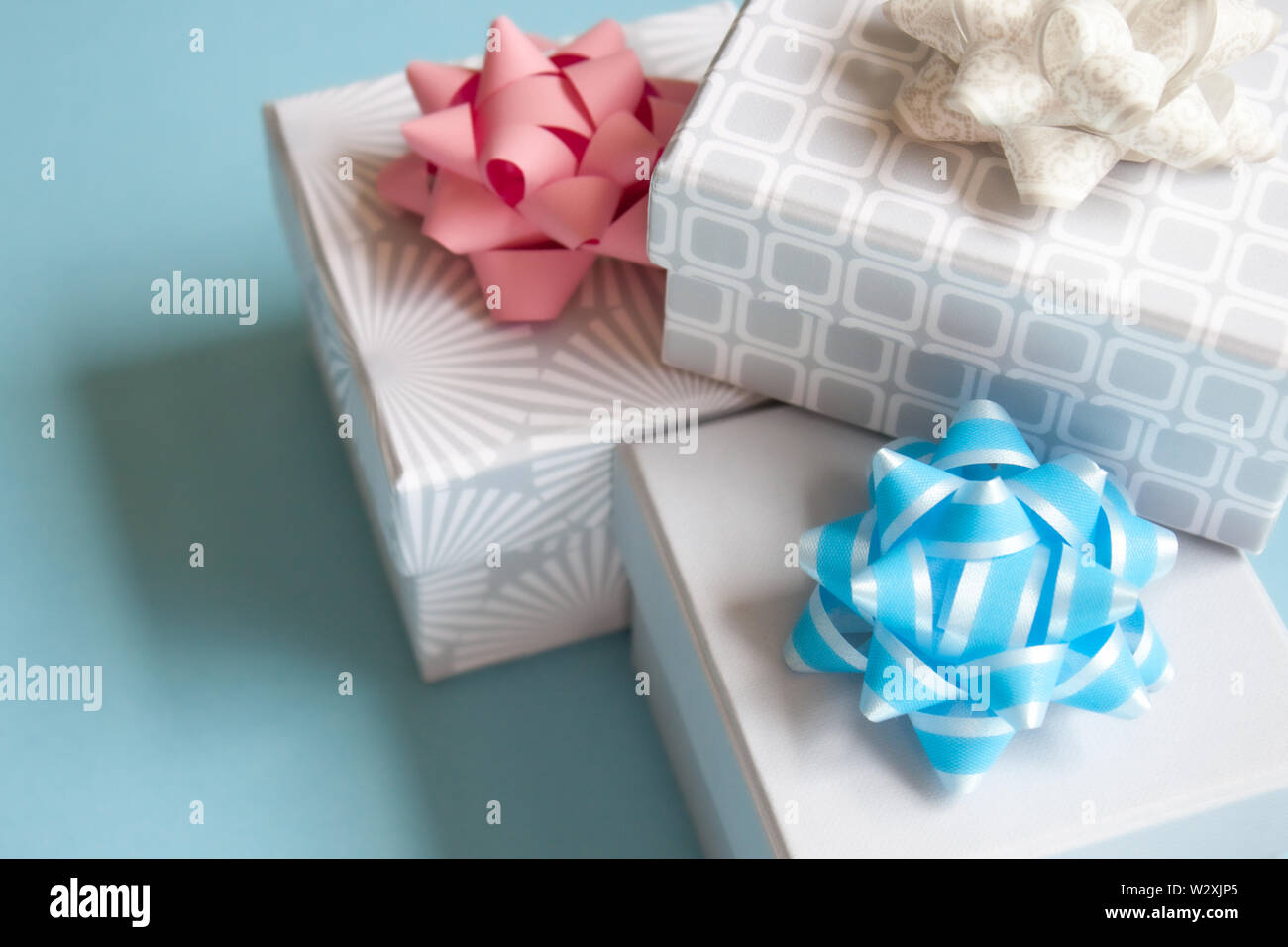 Three light gray gift boxes with light bow on blue background. Festive concept. Stock Photo