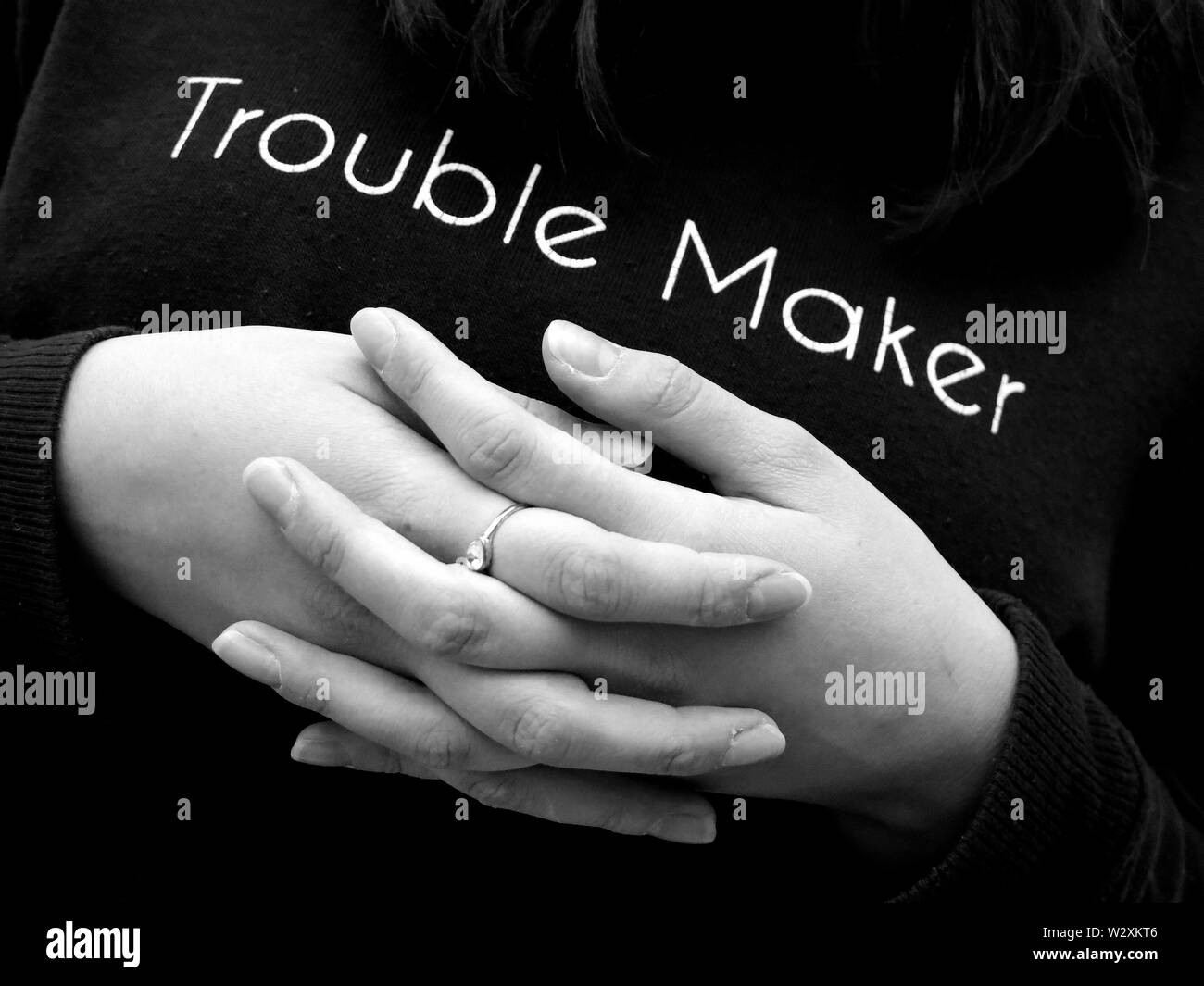 Teenaged girl with hands crossed wearing 'trouble maker' jumper. (Juxtaposition of feelings during adolescence). Stock Photo