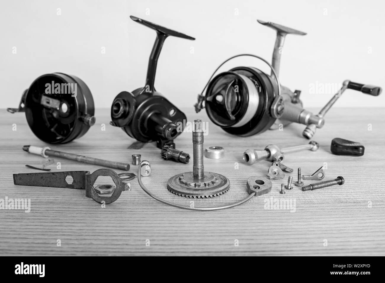A fishing spinning reel as a whole and a second similar completely disassembled. Black and white image. Stock Photo