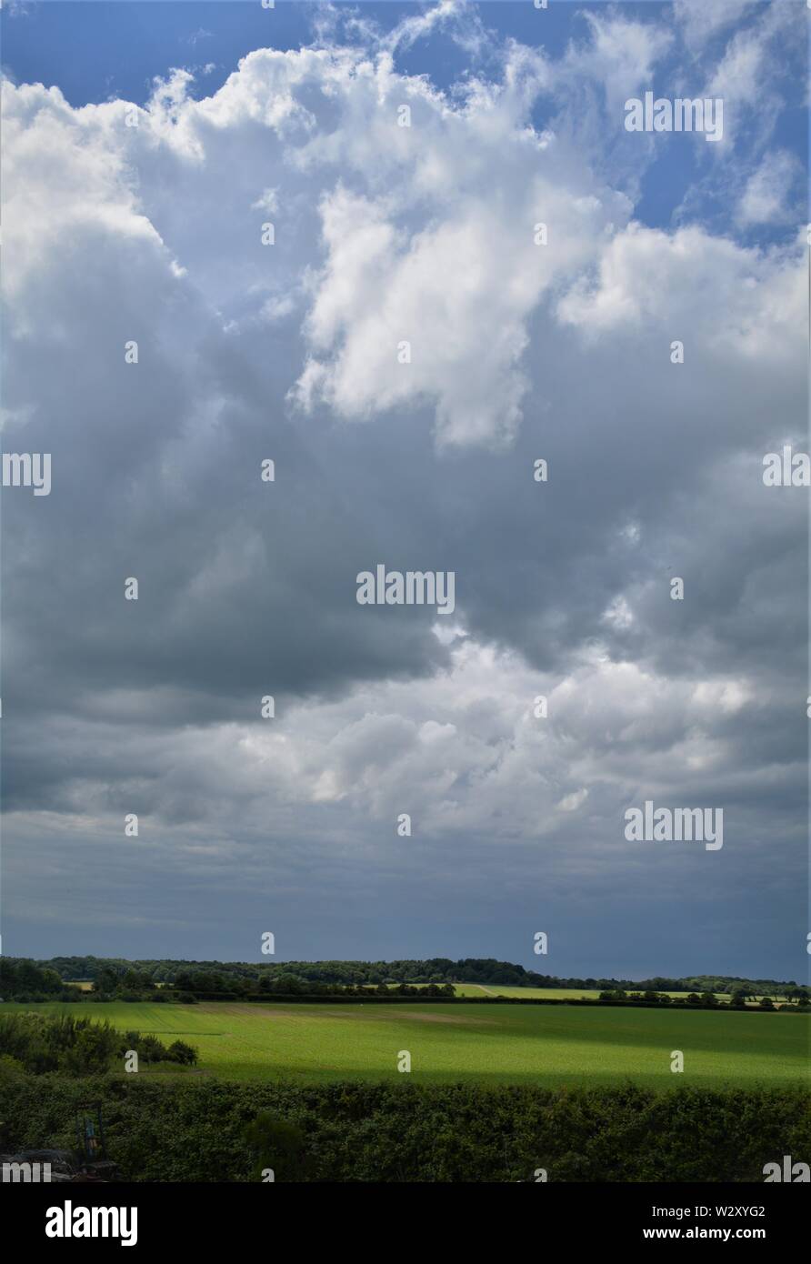 big grey and white clouds looming over green fields by the coast. English landscape. Stock Photo
