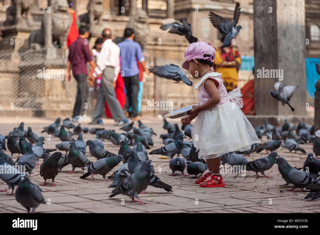 Young girl wearing a pretty dress feeding pigeons in a Temple square in Kathmandu Stock Photo