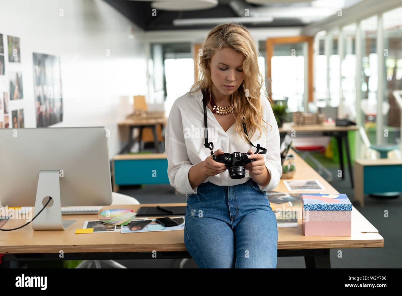 Female graphic designer reviewing photos on digital camera at desk Stock Photo