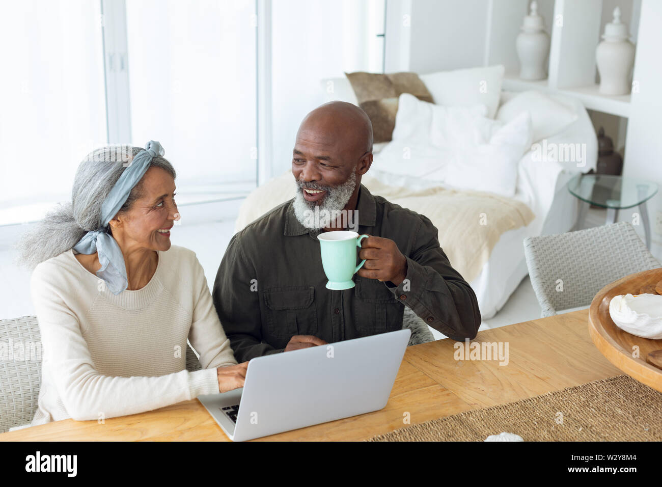 Couple using white laptop on table while man holds a cup Stock Photo