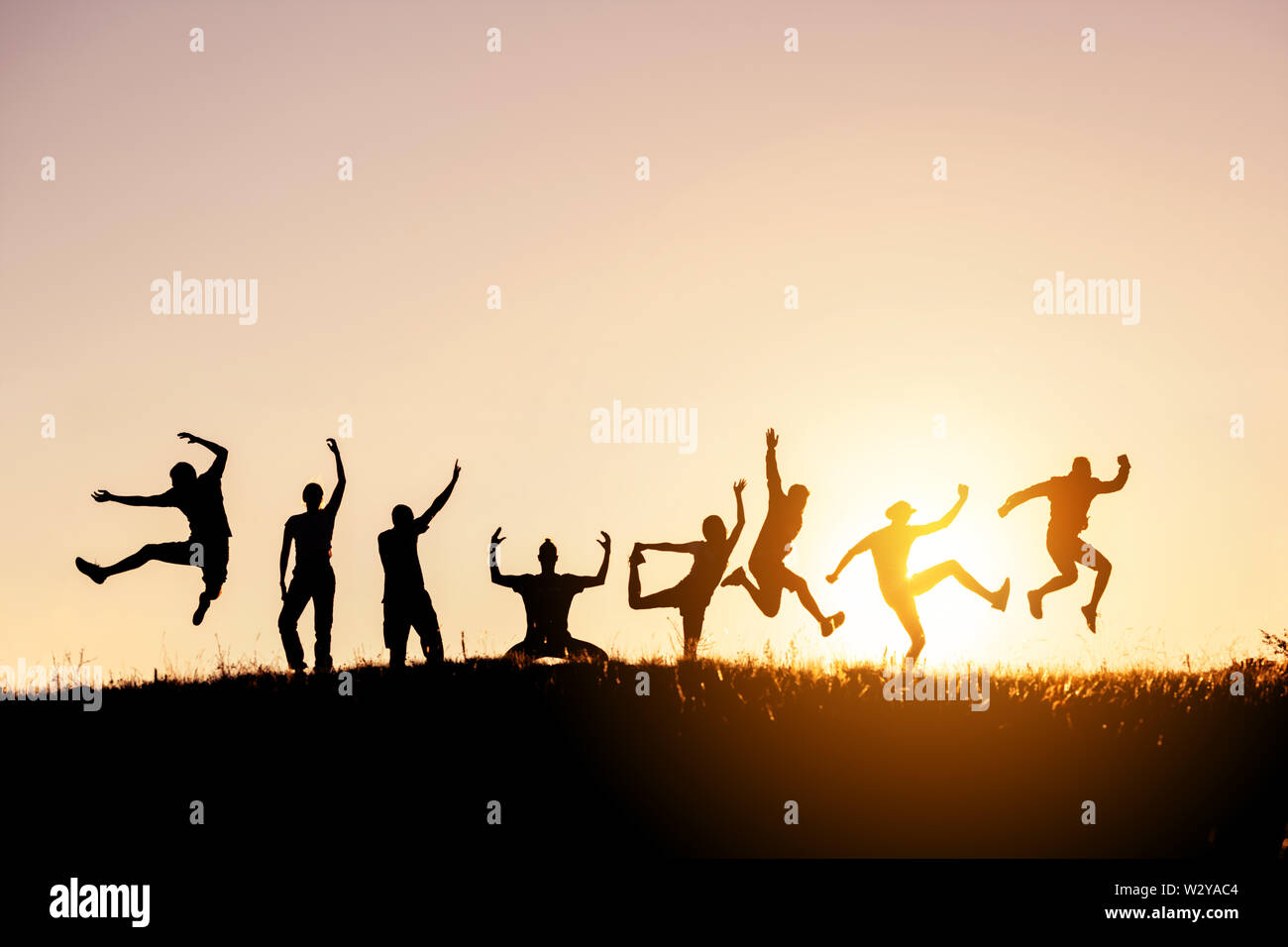 Silhouettes of big group of happy friends jumps and having fun against sunset sky Stock Photo
