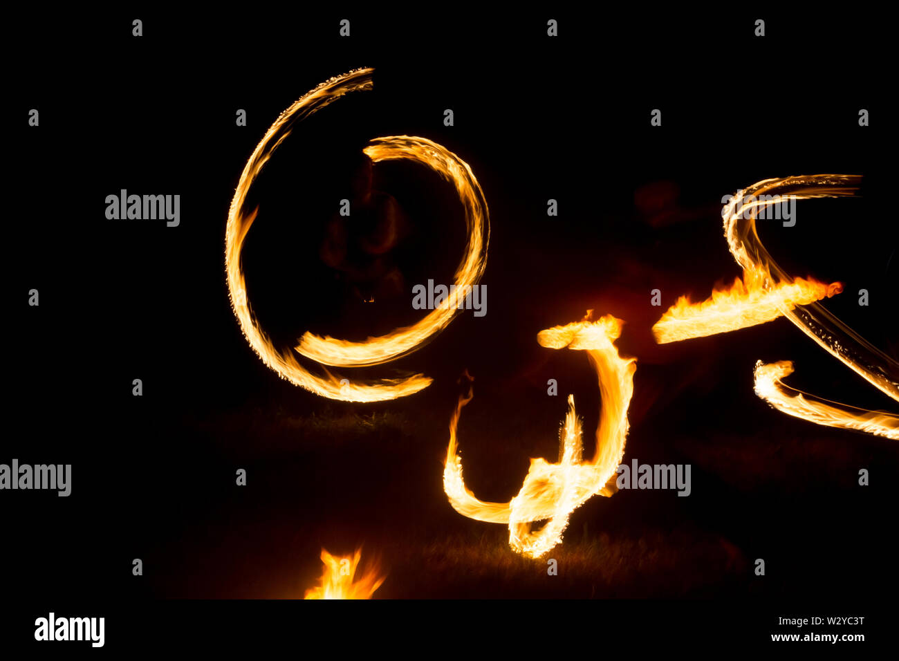 An artist shows a fire show at night spinning torches, circles of fire ...