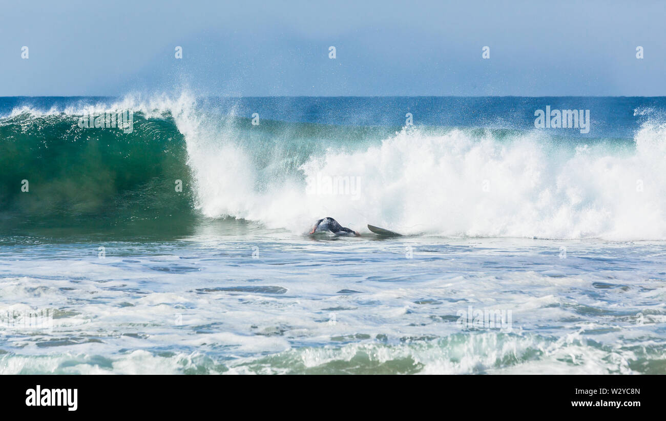 Surfer surfing ride crashing wipe out head under water off surfboard front of ocean wave. Stock Photo