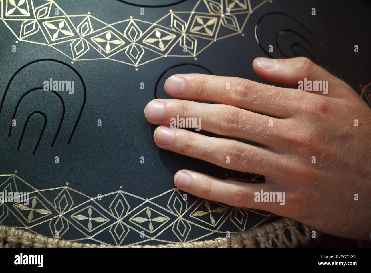 Closeup of a mans hand playing on modern musical instrument Hand pan or Vadjraghanta or metal tongue drumon, selective focus Stock Photo