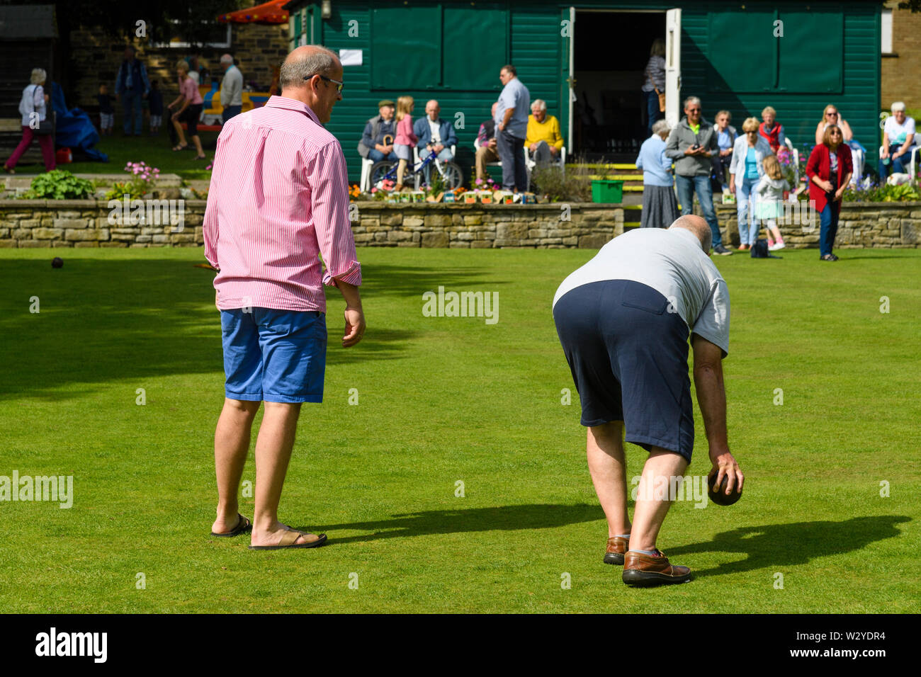 2 men playing target bowls on bowling green at busy fun event (man about to bowl, people watching) - Burley-In-Wharfedale, West Yorkshire, England, UK Stock Photo