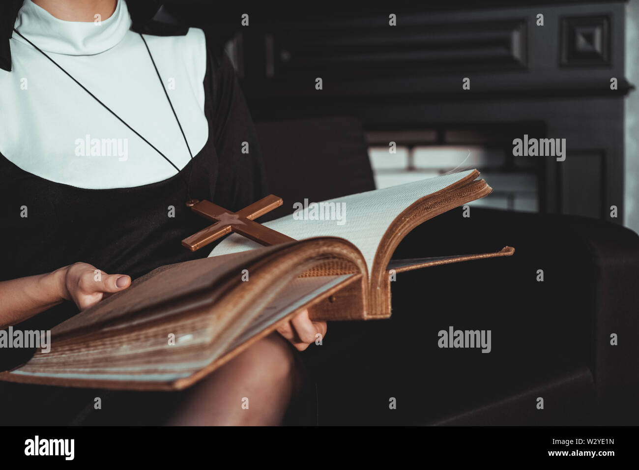 Nun in religion black suit holds Bible and posing on camera with big book on a black background. Close-up. Religion concept. Stock Photo