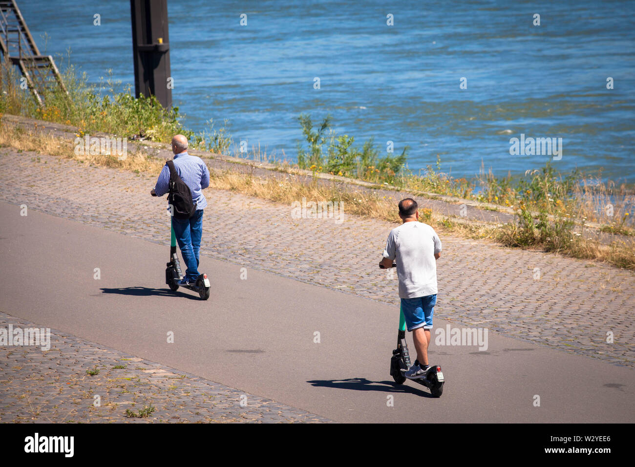 men on a rental electric scooteron the banks of the river Rhine, Cologne, Germany.  Maenner auf Miet-Elektroscooter am Rheinufer, Koeln, Deutschland. Stock Photo