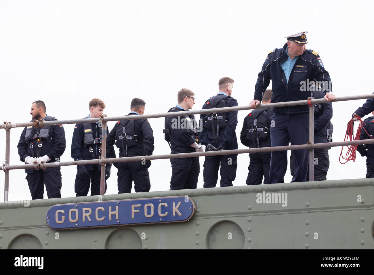 Bern, Germany. 11th July, 2019. Commander Nils Brandt (r) and other crew members are on board when the naval training ship 'Gorch Fock' docks at the Fassmer shipyard. At the shipyard the 'Gorch Fock' is lifted out of the water. In an assembly hall, workers from the Elfleth shipyard are making further progress with the restoration of the ship. Credit: Jörg Sarbach/dpa/Alamy Live News Stock Photo