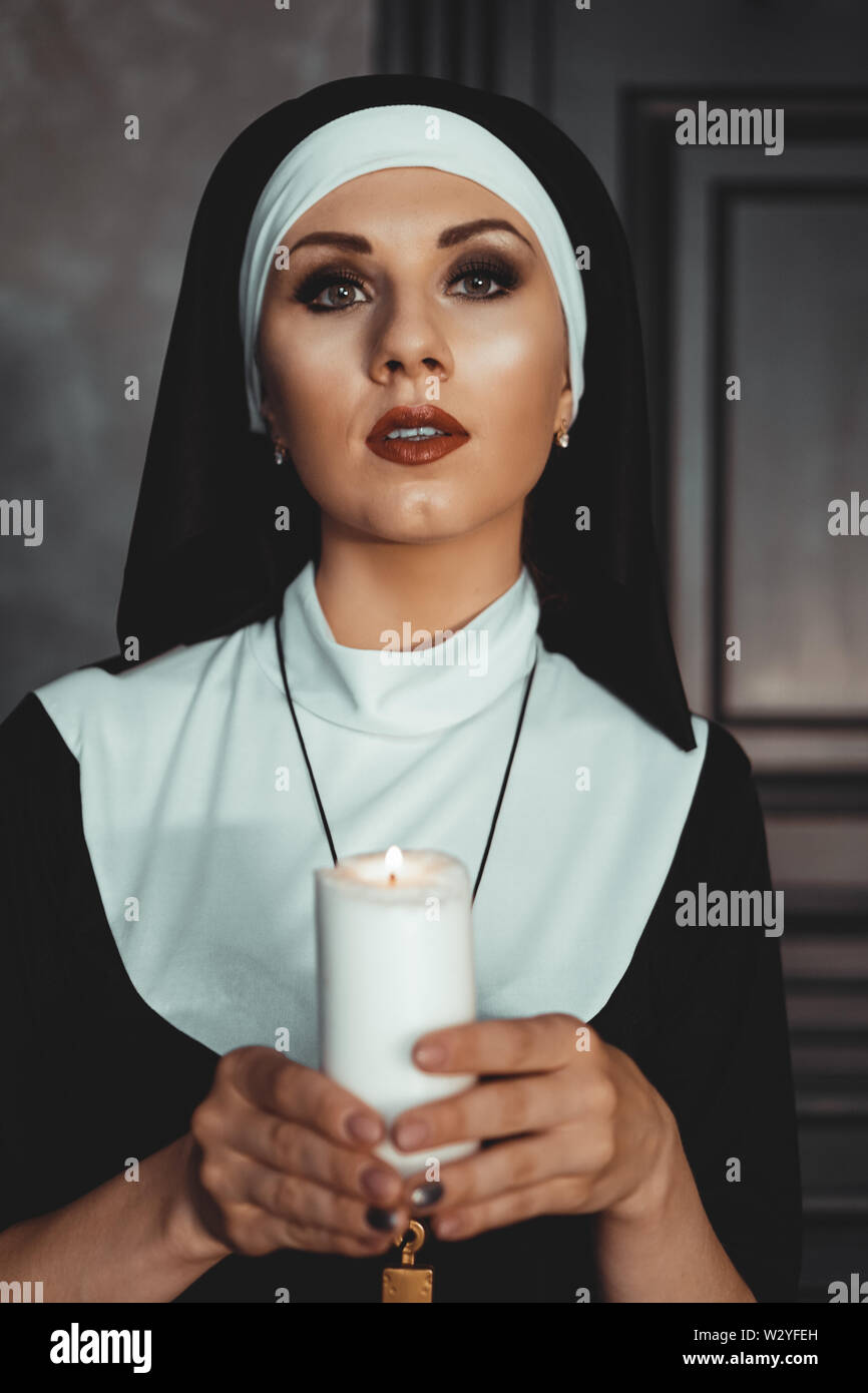 Young catholic nun is holding candle in her hands. Photo on black background. Portrait of beautiful woman Stock Photo