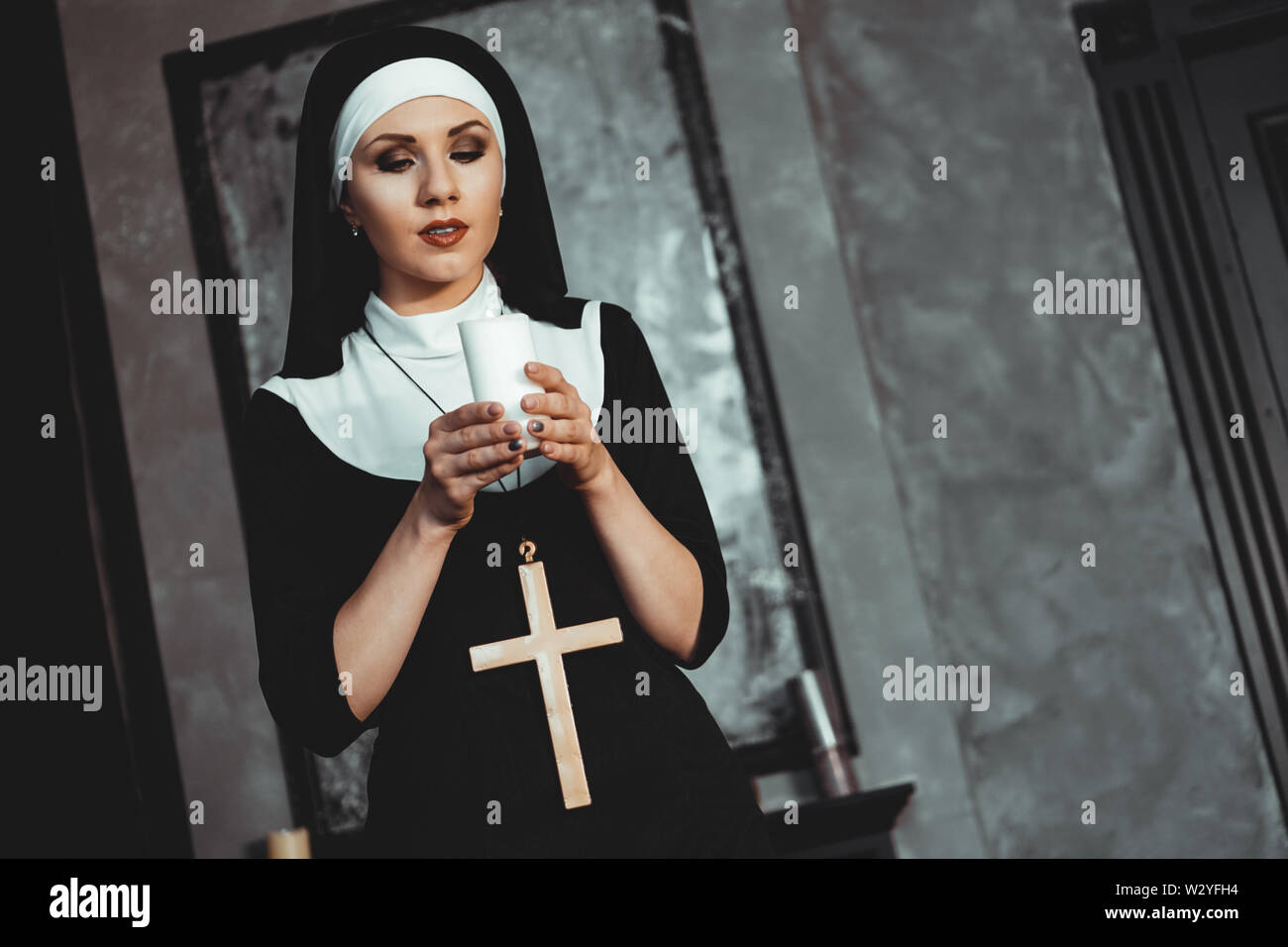 Young catholic nun is holding candle in her hands. Photo on black background. Side view. Stock Photo