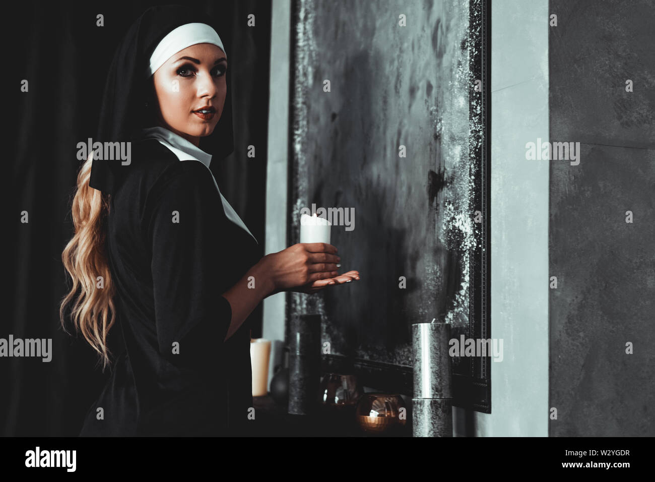 Young catholic nun is holding candle in her hands. Photo on black background. Side view. Stock Photo