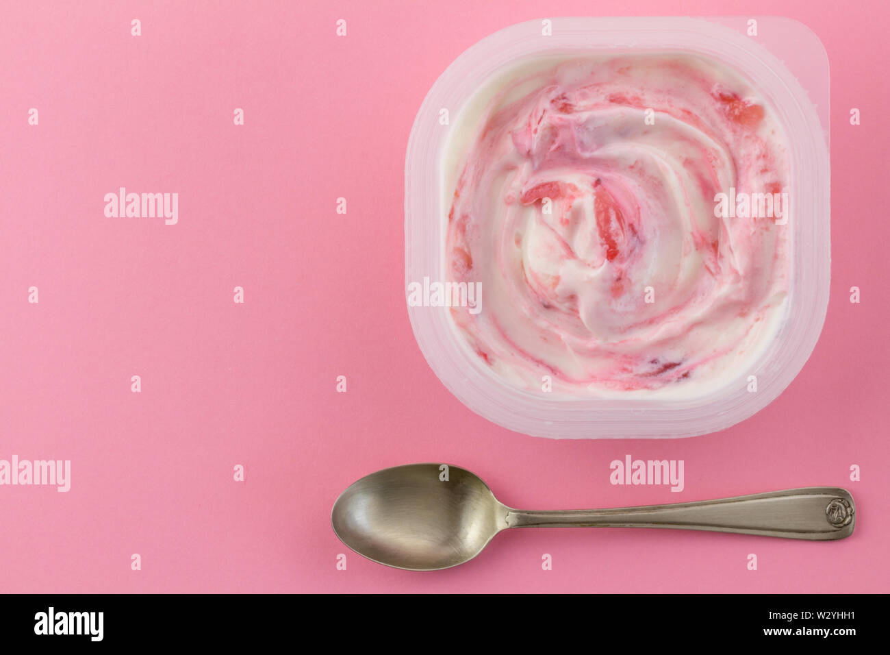 Yogurt cup with natural strawberry greek style yogurt swirled with real strawberries isolated on light pink background with small silver spoon - top v Stock Photo