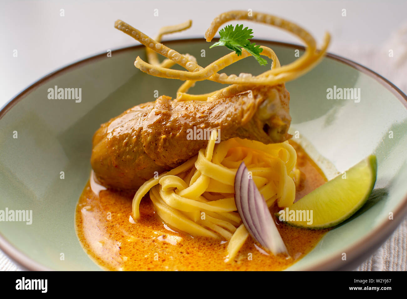 thai yellow chicken drumsticks curry with fresh egg noodles , lime, coriander and crispy fried egg noodles in a plated dish Stock Photo