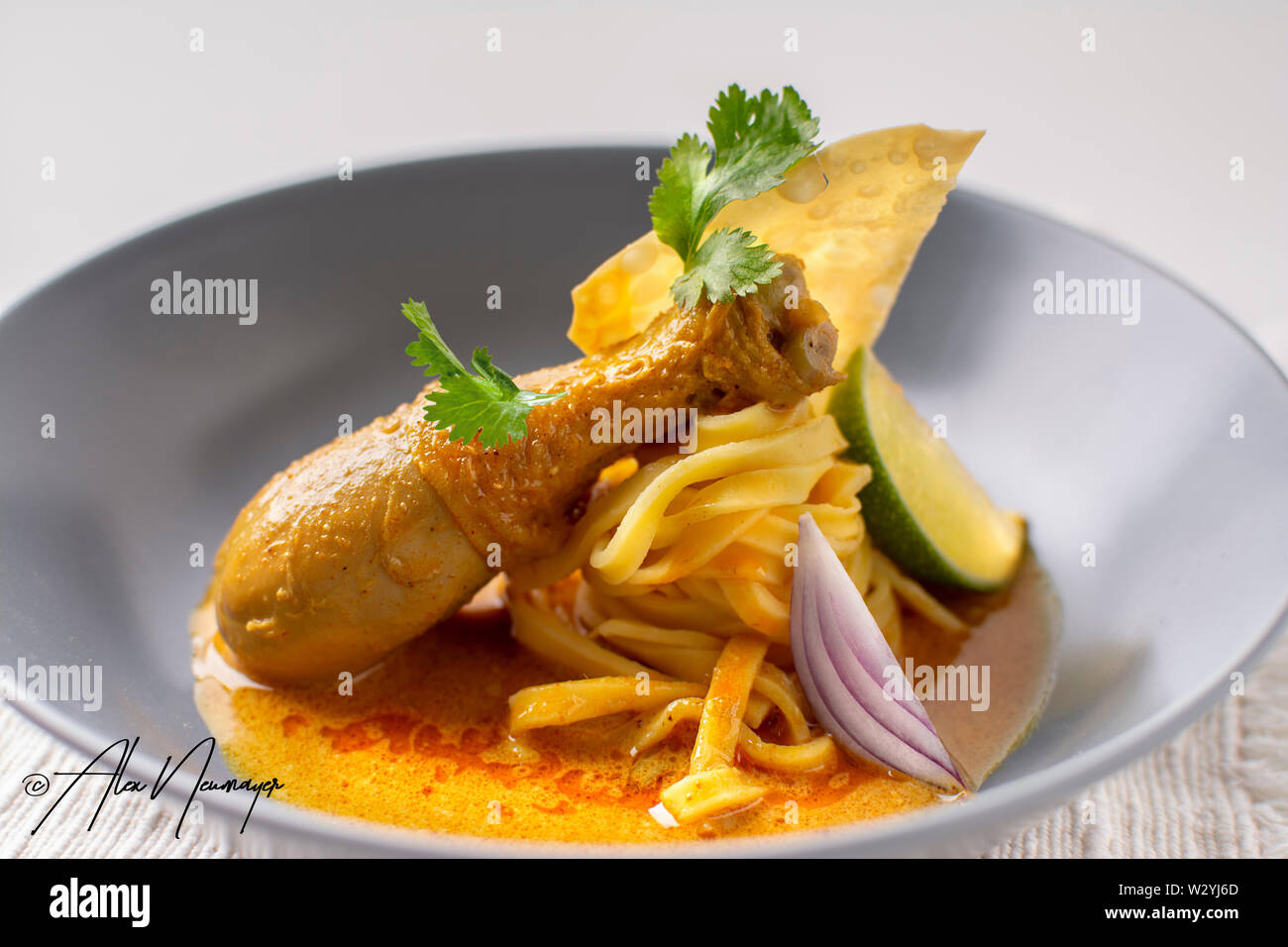 thai yellow chicken drumsticks curry with fresh egg noodles , lime, coriander and crispy fried egg noodles in a plated dish Stock Photo