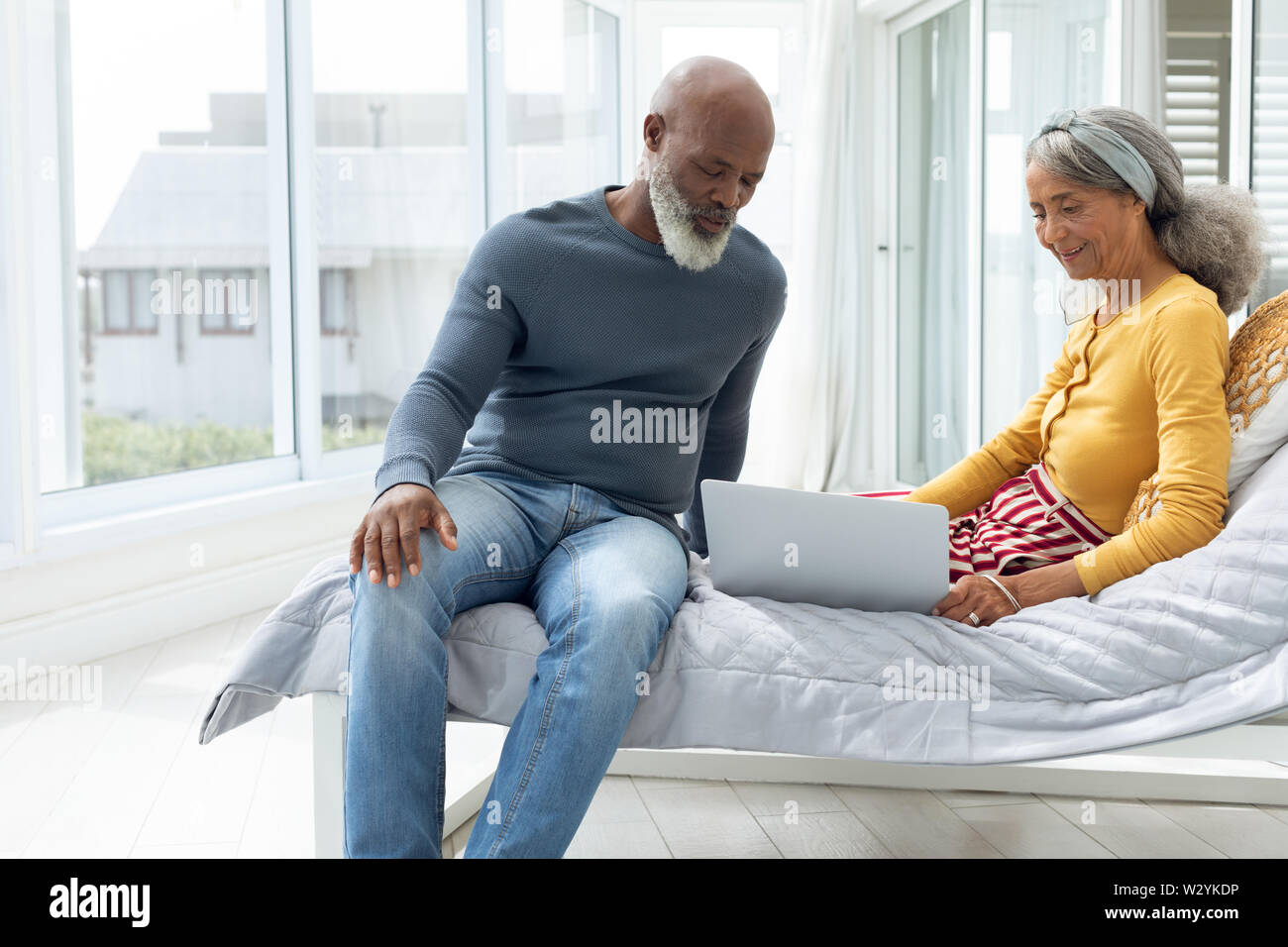 Couple sitting on a bed while using a laptop Stock Photo