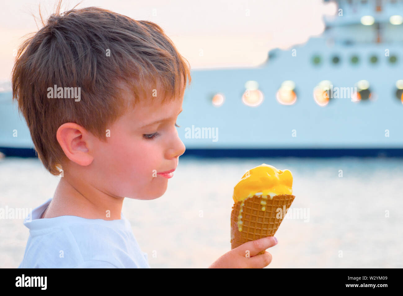 Boy with ice-cream with yacht on background. Sweet food background. Child eating ice-cream on seashore with ferry boat on background. Sweet life Stock Photo