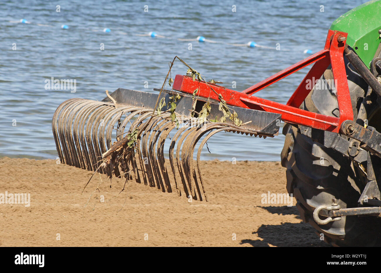 Tractor with large metal rake attached sifting, raking and clearing debris at a public beach in early morning Stock Photo