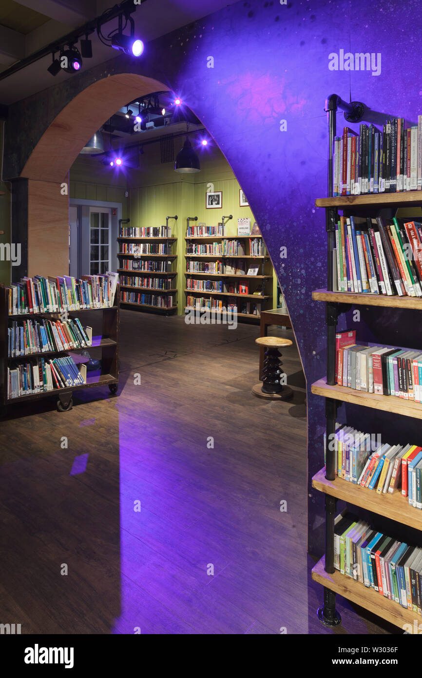 Purple spotlit wave-form wall section in children's library, with bookshelves. Deichman Library Grunerlokka, Oslo, Norway. Architect: Aat Vos, 2019. Stock Photo