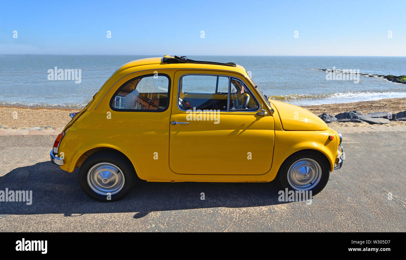 Classic  Yellow Fiat 500 parked on seafront promenade. Stock Photo