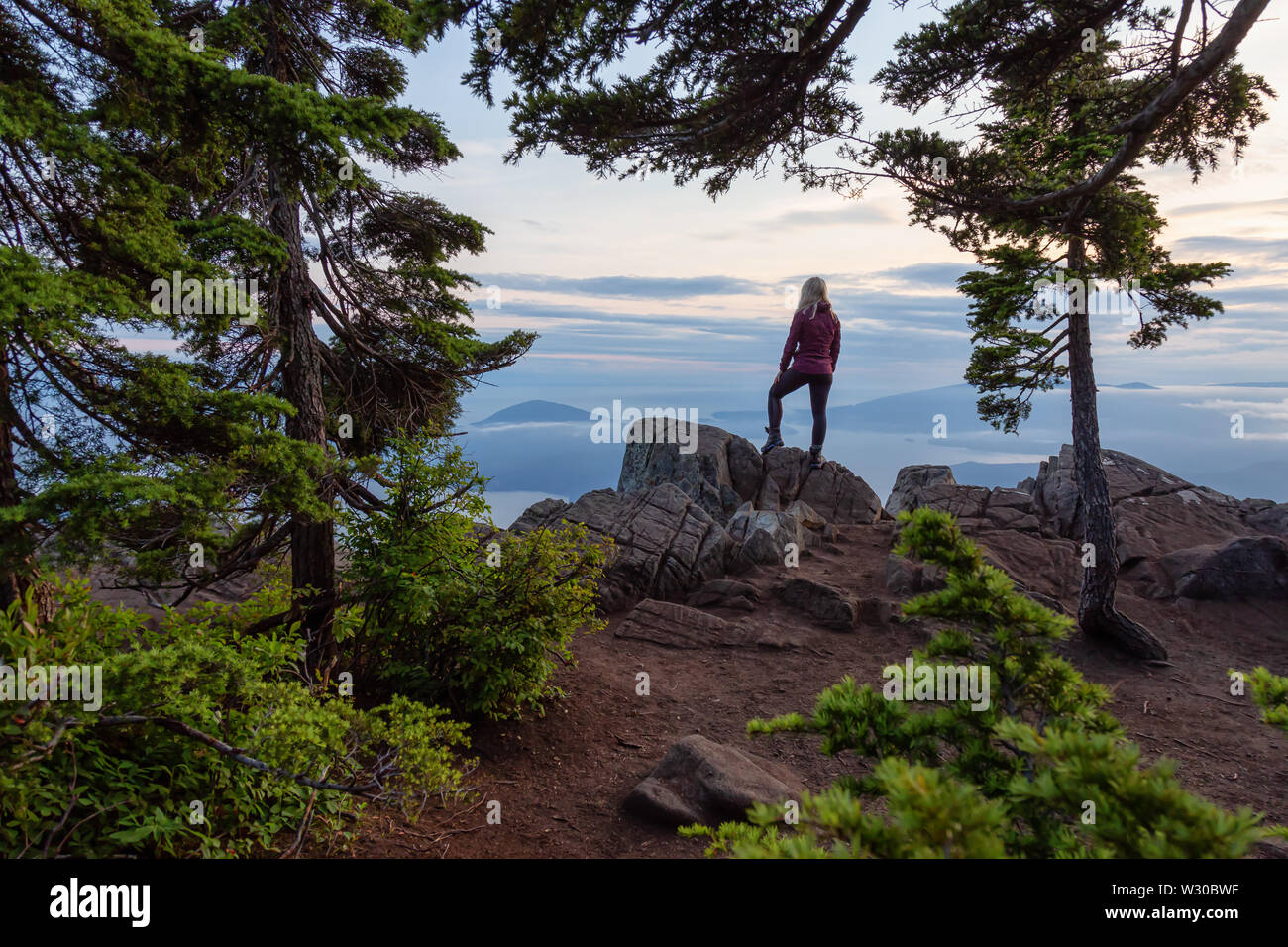 Female Hiker on top of a mountain covered in clouds during a vibrant summer sunset. Taken on top of St Mark's Summit, West Vancouver, British Columbia Stock Photo
