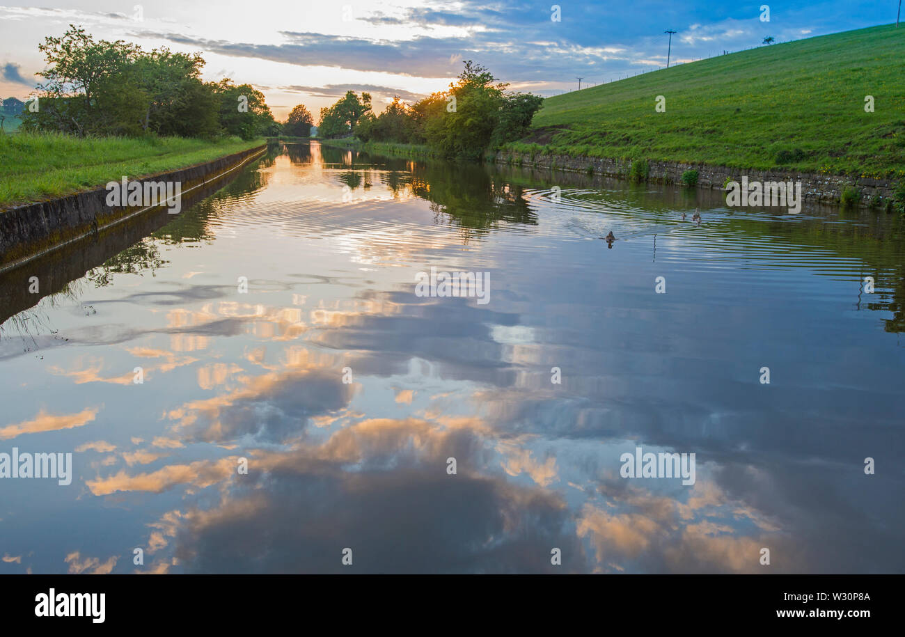 View of an English rural countryside scenery on British waterway canal during overcast cloudy day at sunset dusk Stock Photo