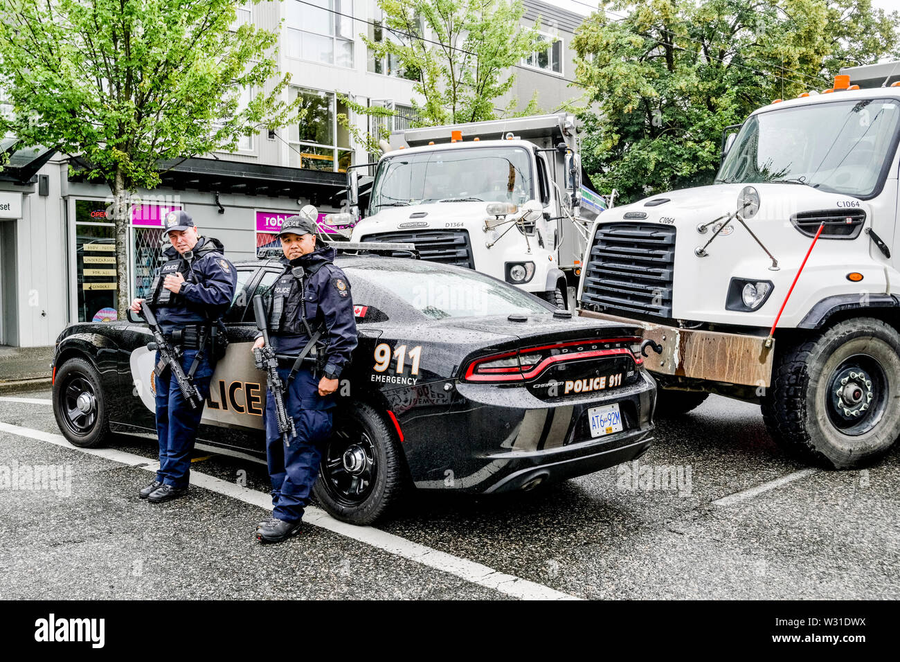 Police with automatic weapons and dump trucks guard access to Commercial Drive, Car Free Day,  Vancouver, British Columbia, Canada Stock Photo