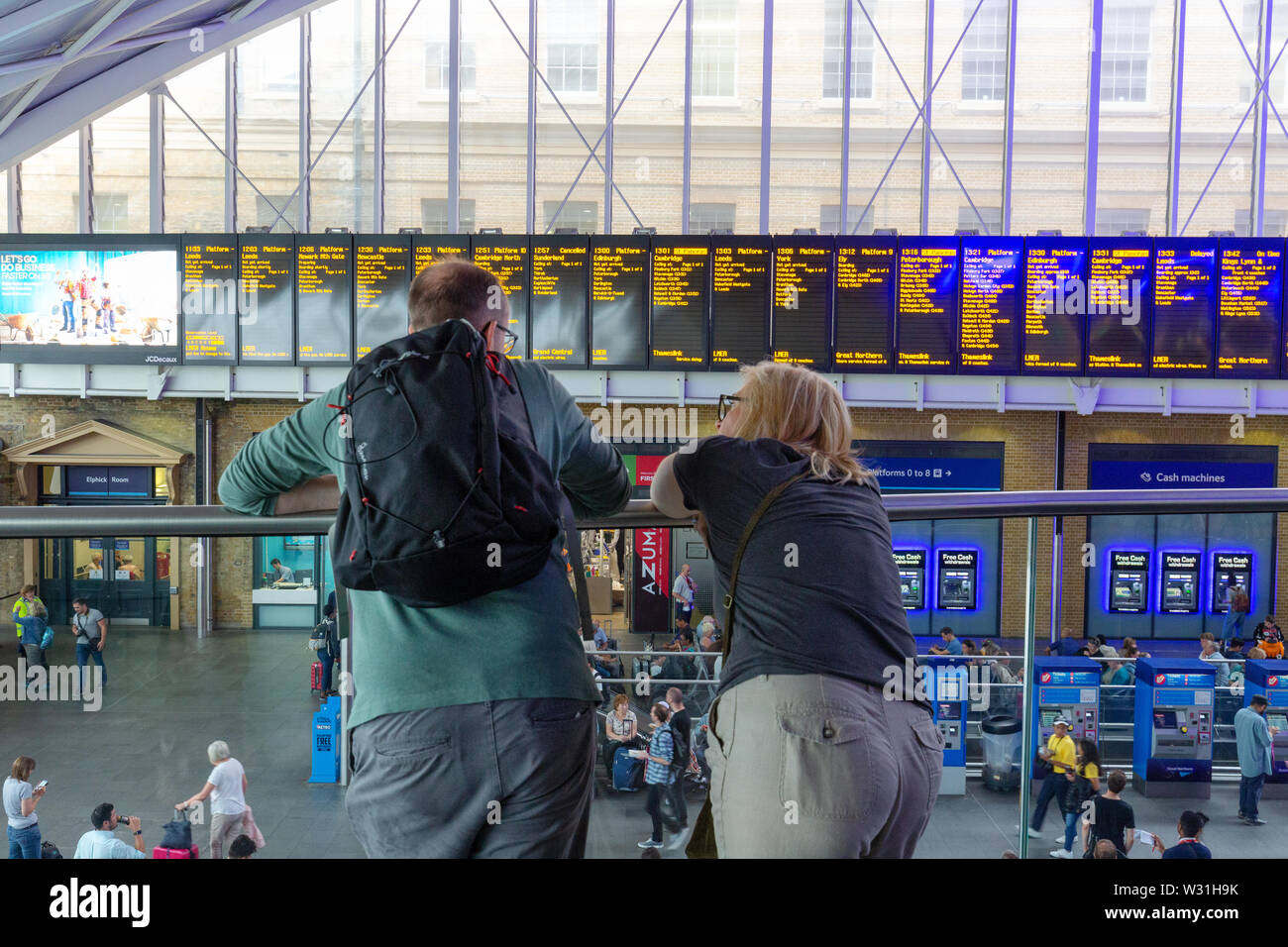 Kings Cross station London: a couple of rail passengers looking at the train departure board from the concourse, Kings Cross train station, London UK Stock Photo