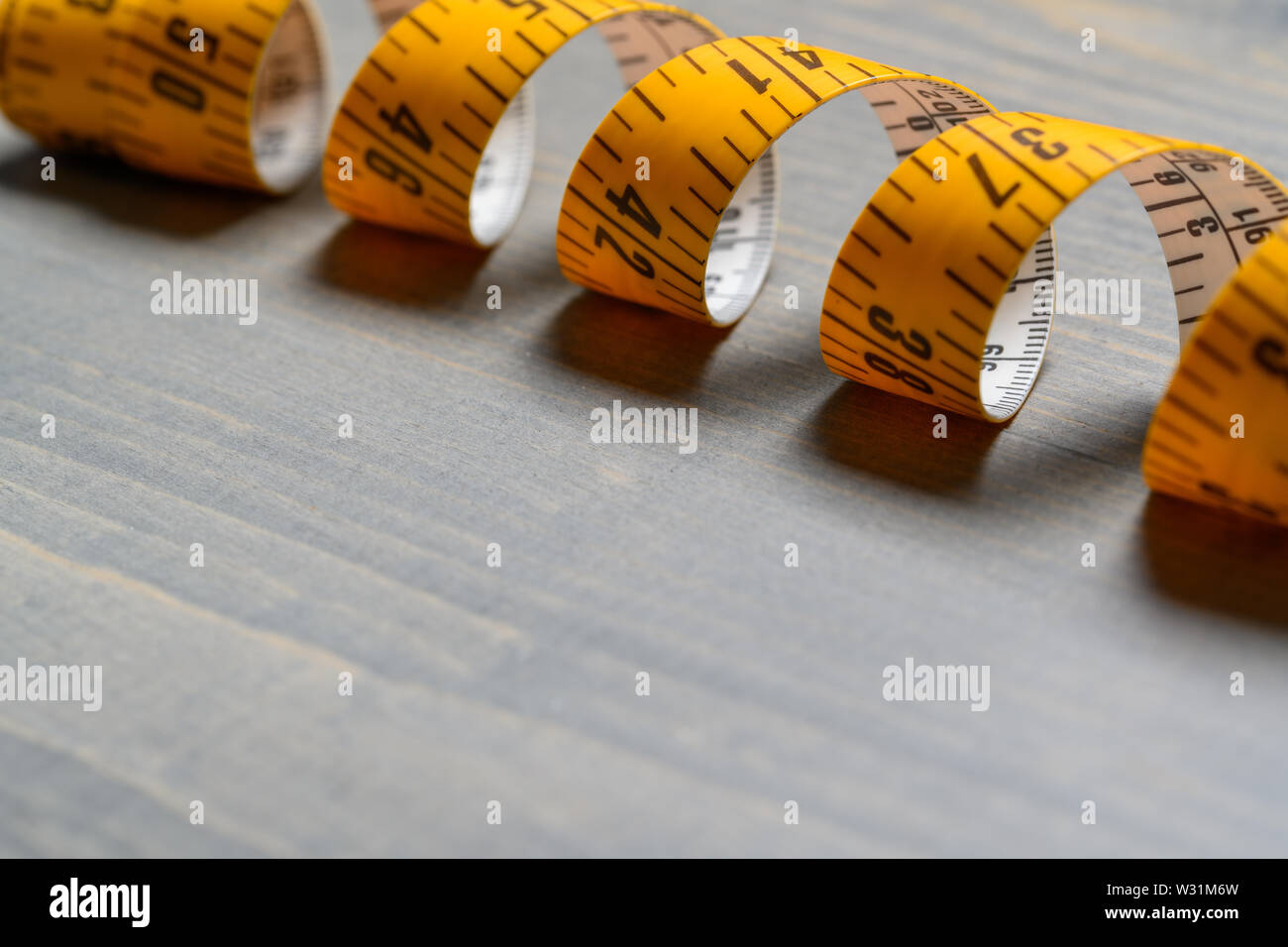 Yellow Tailor measuring tape on wooden table back Stock Photo